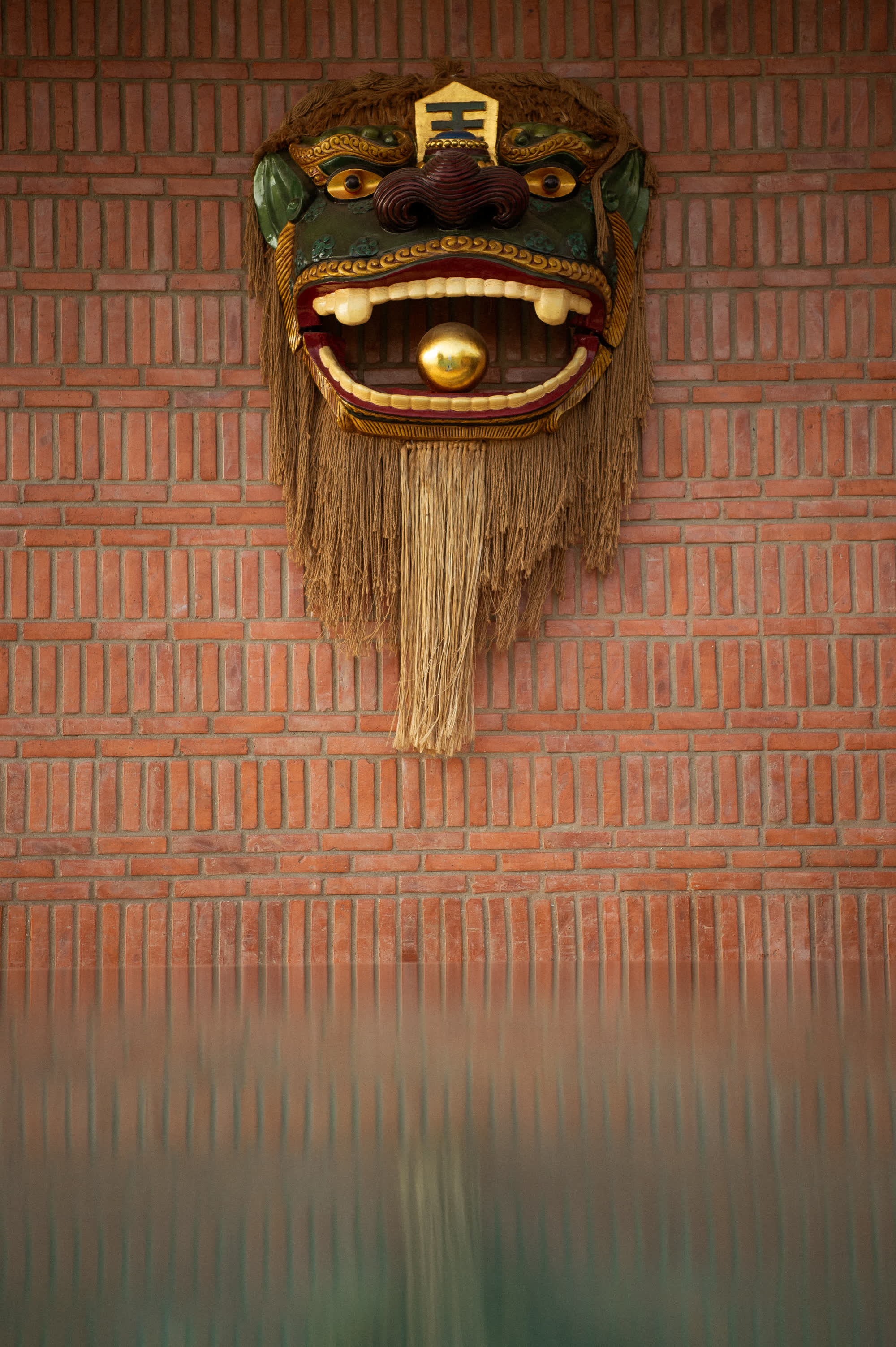 The gilded Nghê mask with its fibre beard on the brick wall above the pool bar at Nghê Prana