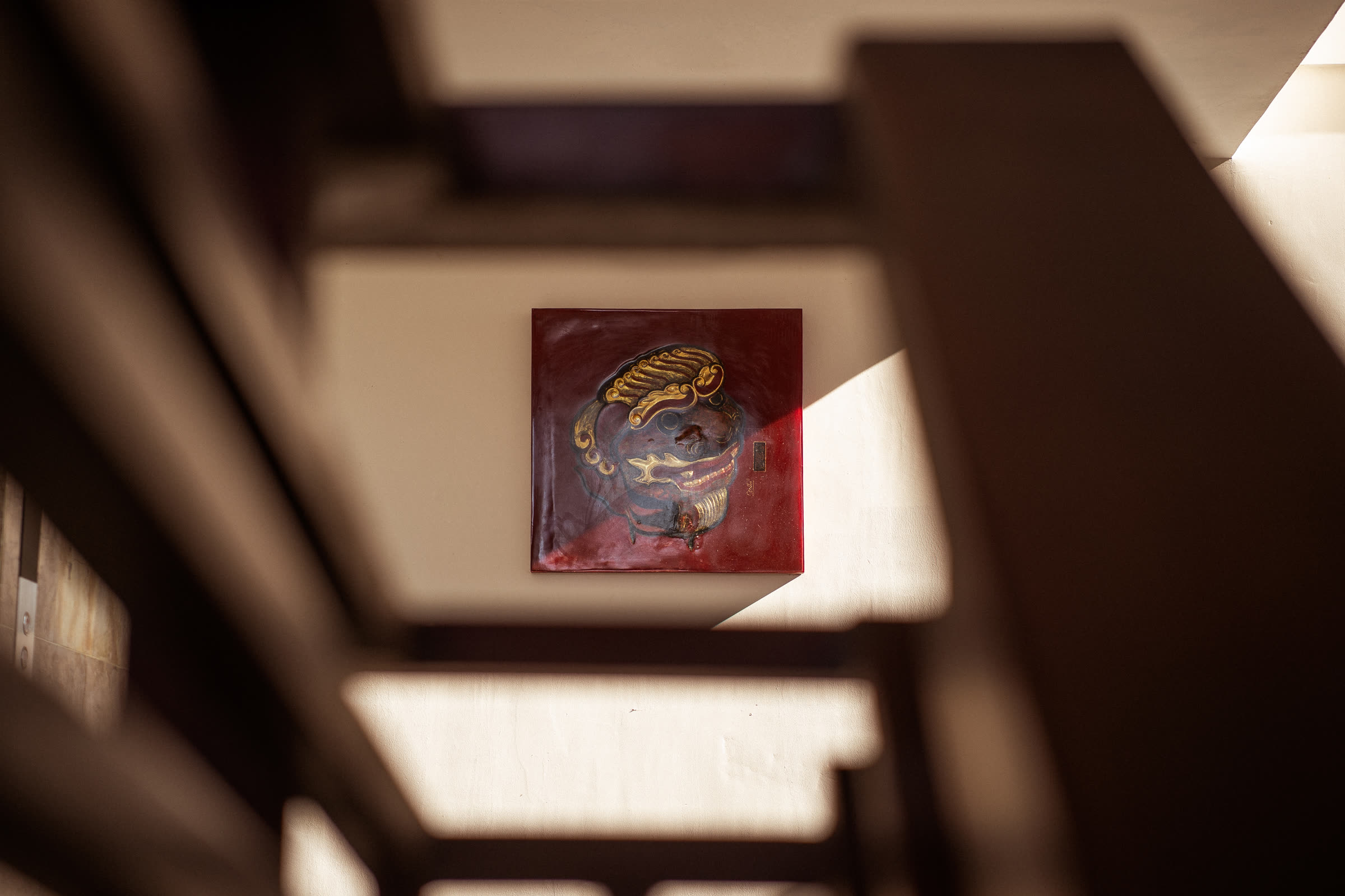 A red lacquer Nghê plaque set into the stairwell wall at Nghê Prana, Hội An