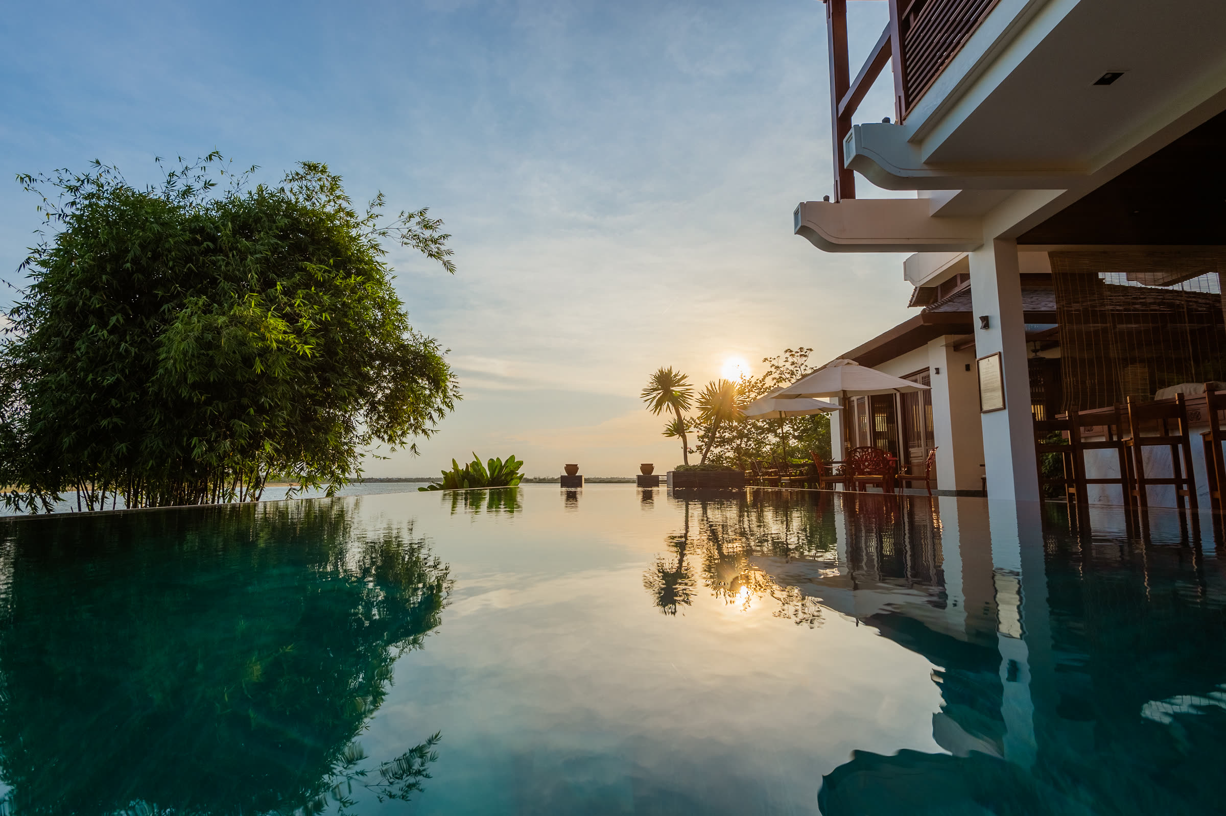 The infinity pool at Nghê Prana at sunset, its edge level with the Thu Bồn River
