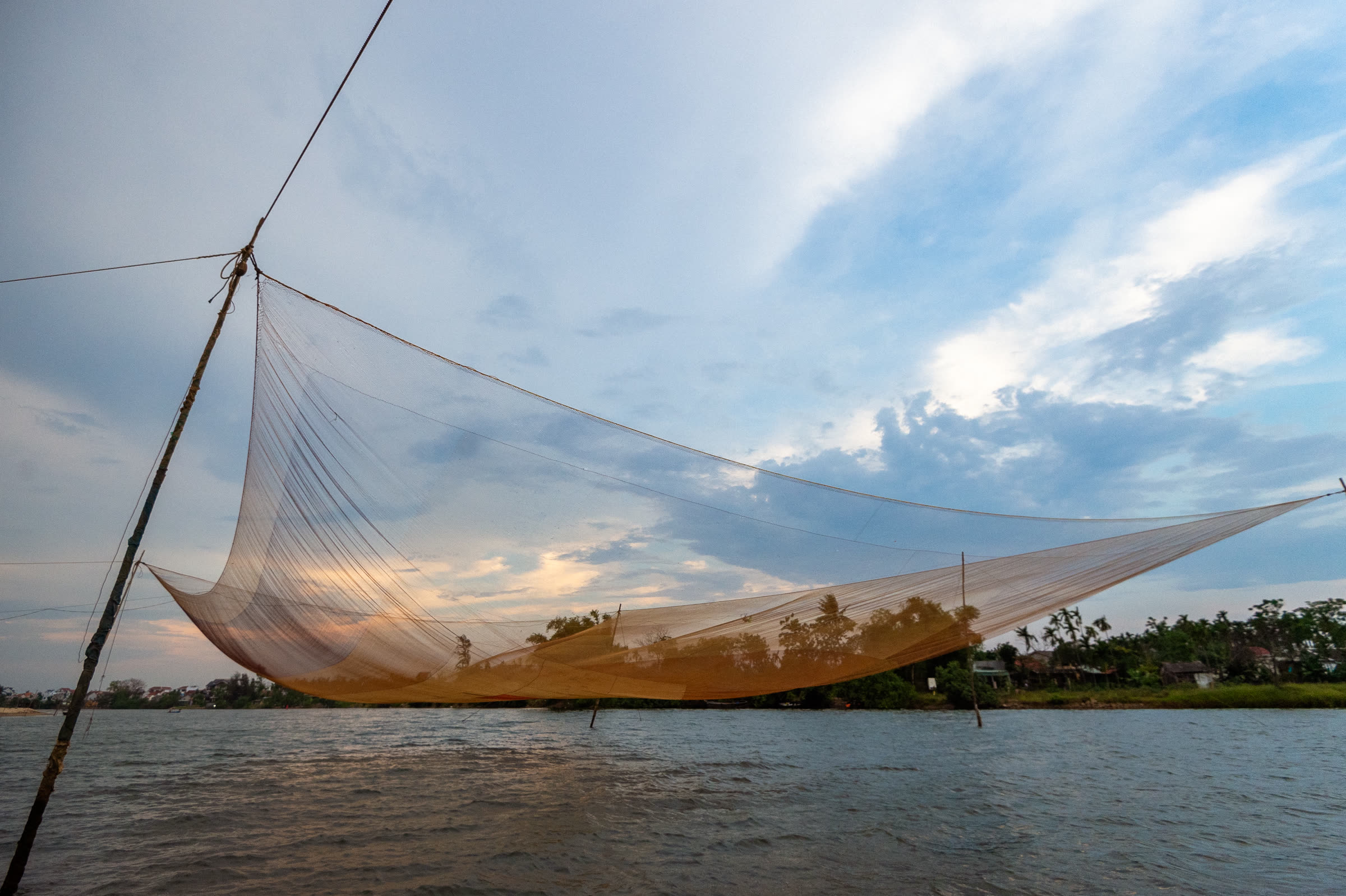 A Vietnamese square dip net raised over the Thu Bồn River at sunset near Hội An