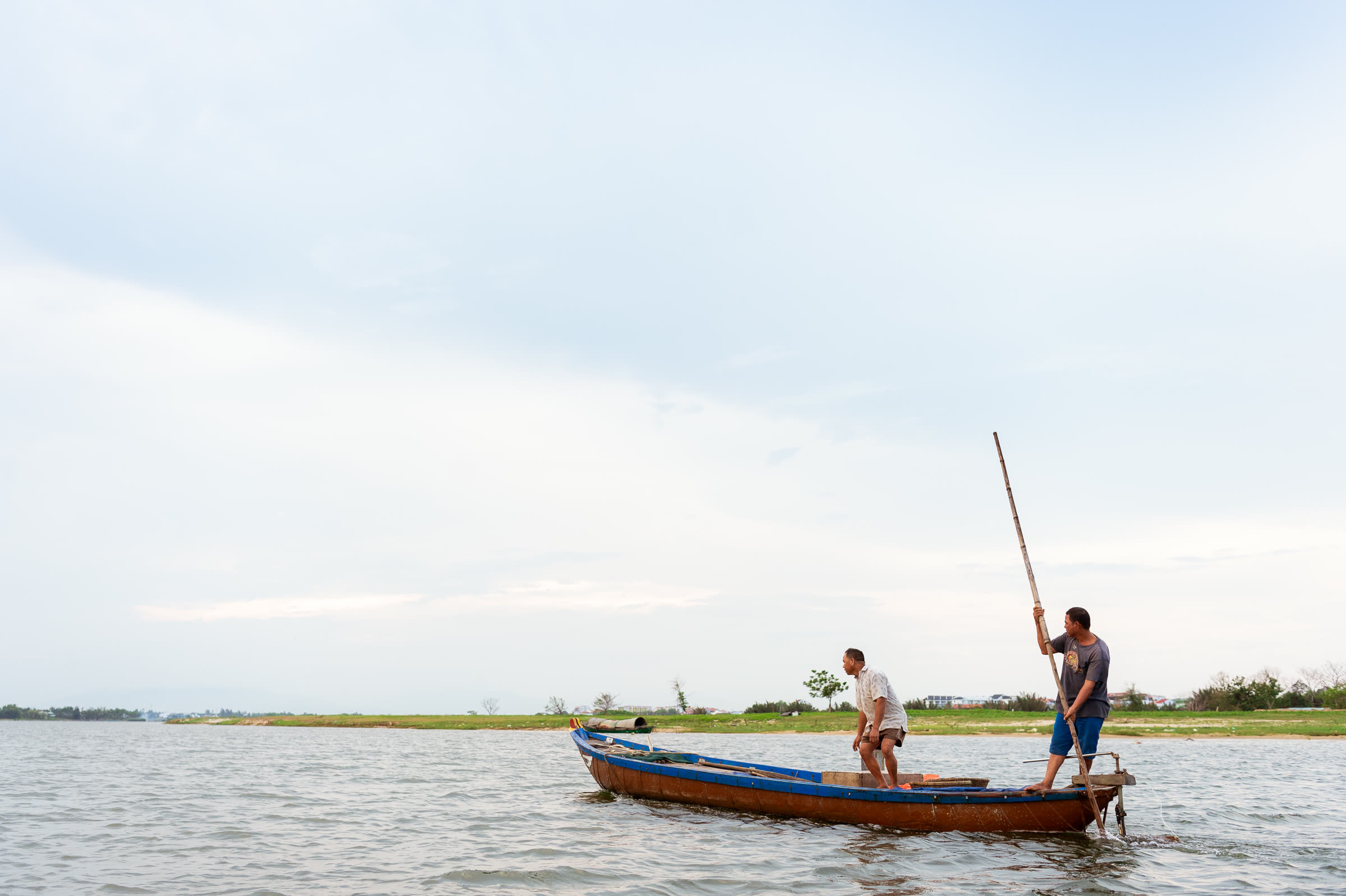 Fishermen poling a wooden boat along the Thu Bồn River at Hội An
