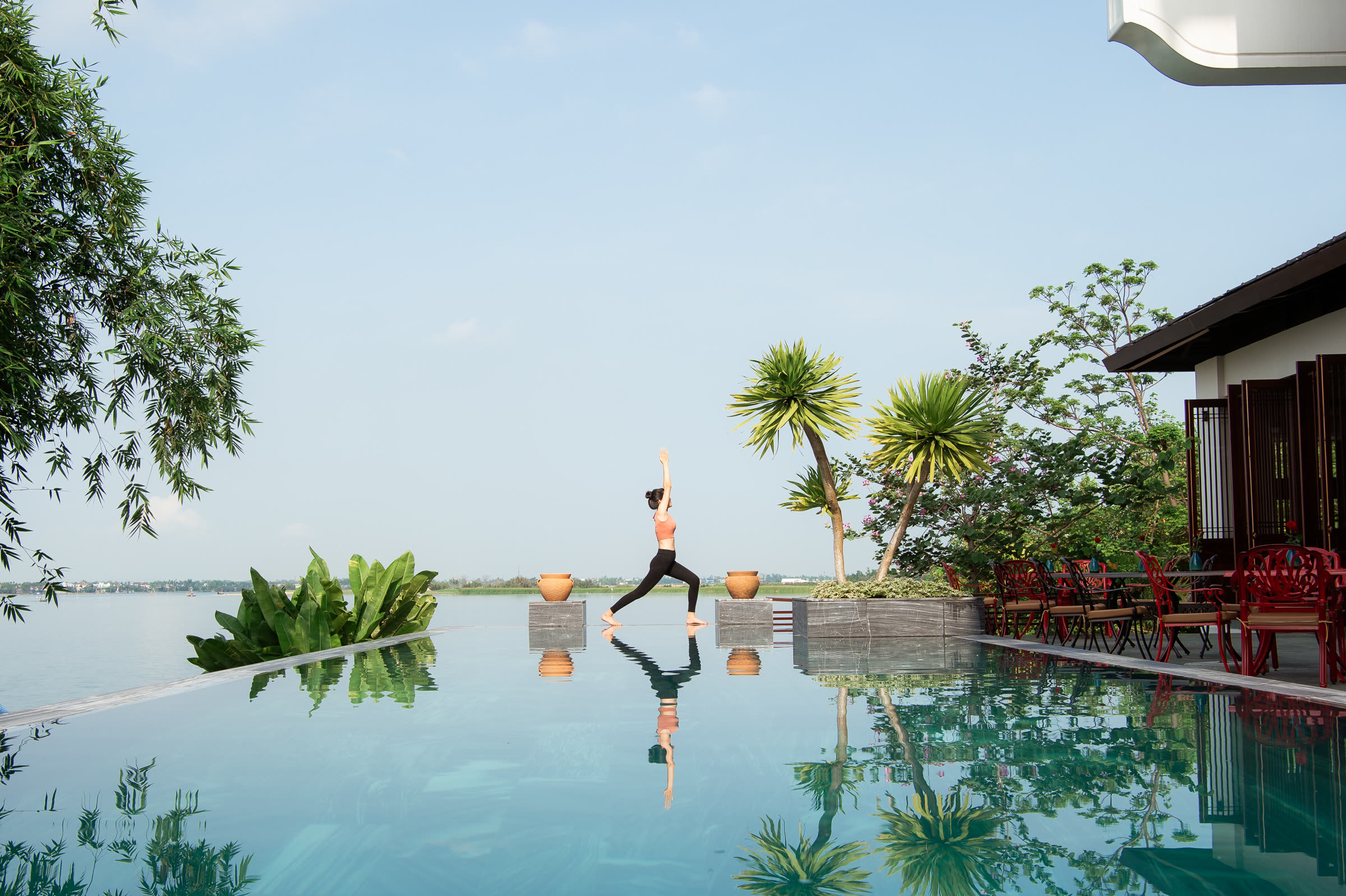Warrior pose on the pool deck at Nghê Prana, reflected in the still water of the infinity pool